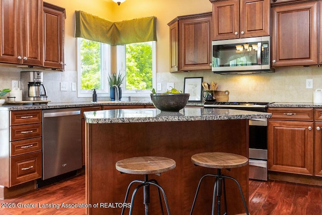 4655 Dimond Way, Dimondale, MI 48821 - kitchen featuring stainless steel appliances, dark wood finished floors, a center island, and dark stone countertops