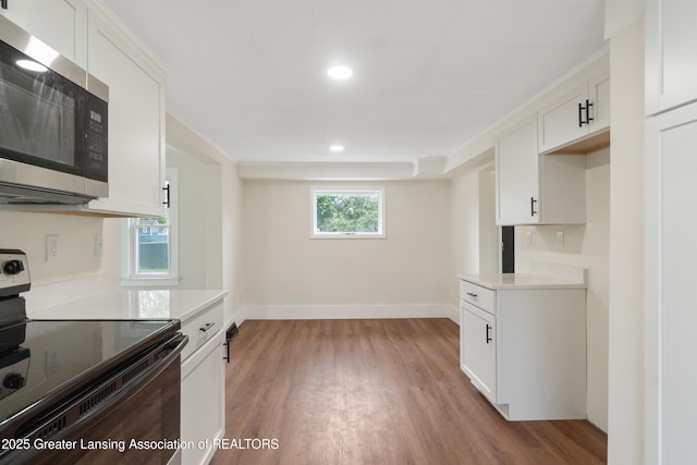 828 Backus St, Jackson, MI 49202 - kitchen featuring black / electric stove, stainless steel microwave, light wood finished floors, white cabinetry, and light countertops