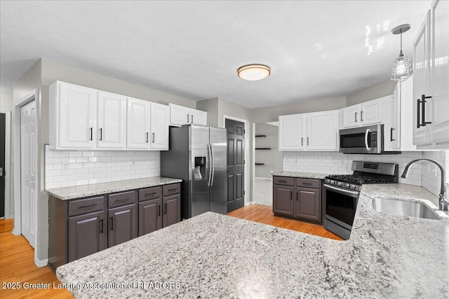 5859 Printemp Dr, East Lansing, MI 48823 - kitchen with appliances with stainless steel finishes, a sink, light wood-style flooring, white cabinetry, and a textured ceiling