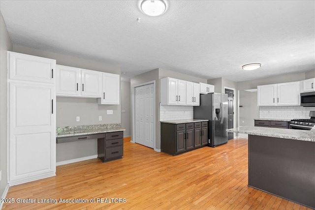 5859 Printemp Dr, East Lansing, MI 48823 - kitchen with stainless steel appliances, white cabinets, backsplash, light wood-style flooring, and a textured ceiling