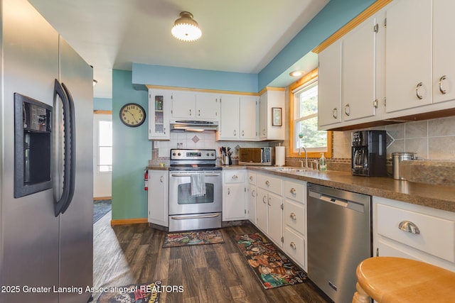 6391 Lakeshore Dr, Lakeview, MI 48850 - kitchen with stainless steel appliances, under cabinet range hood, dark wood-type flooring, white cabinetry, and decorative backsplash
