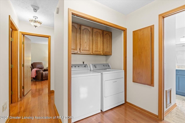 3720 Lott Ave, Holt, MI 48842 - washroom with cabinet space, washer and clothes dryer, light wood-style flooring, a textured ceiling, and baseboards