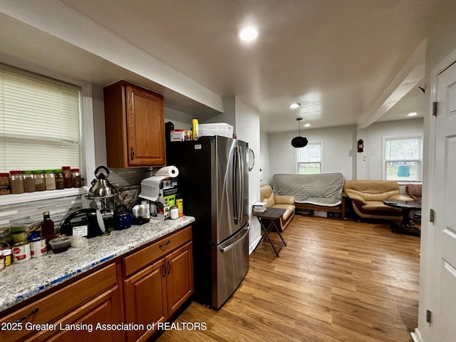 1916 W Jolly Rd, Lansing, MI 48910 - kitchen featuring brown cabinetry, light wood finished floors, decorative backsplash, open floor plan, and freestanding refrigerator