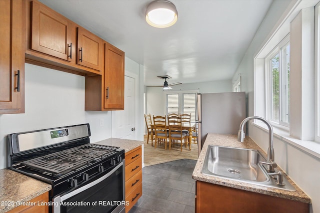 5104 Old Lansing Rd, Lansing, MI 48917 - kitchen featuring stainless steel appliances, a sink, brown cabinetry, a ceiling fan, and dark tile patterned floors