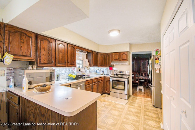 3733 Colchester Rd, Lansing, MI 48906 - kitchen with appliances with stainless steel finishes, under cabinet range hood, light countertops, a peninsula, and a sink