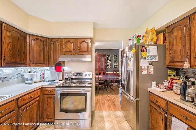 3733 Colchester Rd, Lansing, MI 48906 - kitchen featuring stainless steel appliances, under cabinet range hood, light countertops, tasteful backsplash, and brown cabinetry