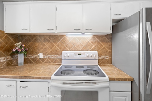 1111 Battle Creek Rd, Charlotte, MI 48813 - kitchen with freestanding refrigerator, electric range, white cabinets, backsplash, and tile counters