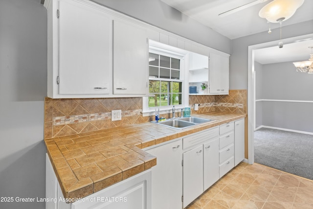 1111 Battle Creek Rd, Charlotte, MI 48813 - kitchen featuring a sink, white cabinets, a chandelier, light carpet, and backsplash