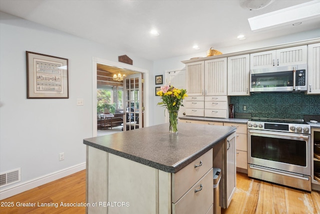 1435 Epley Rd, Williamston, MI 48895 - kitchen with appliances with stainless steel finishes, light wood-type flooring, backsplash, dark countertops, and a chandelier