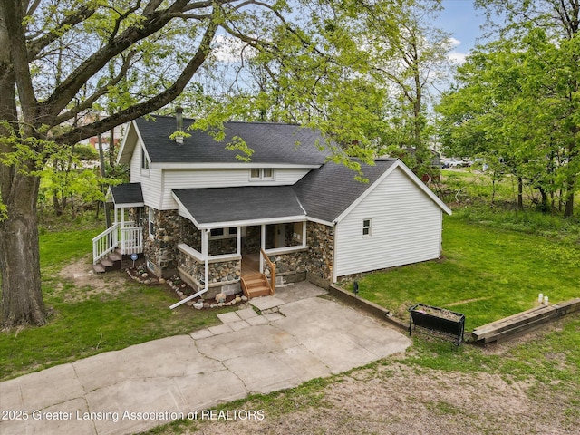 1900 Kaplan St, Lansing, MI 48917 - rear view of property featuring stone siding, covered porch, roof with shingles, a yard, and driveway