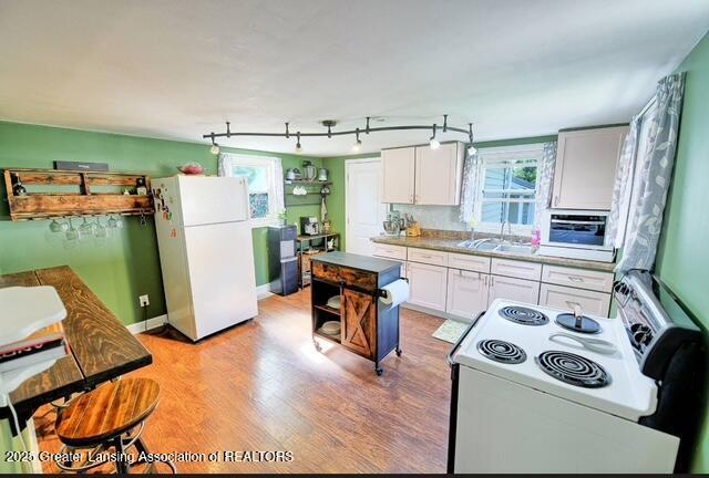 711 W Henry St, Charlotte, MI 48813 - kitchen featuring white appliances, a sink, light wood-style floors, white cabinetry, and rail lighting