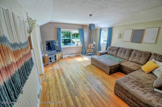711 W Henry St, Charlotte, MI 48813 - living room featuring a wood stove, wood-type flooring, a textured ceiling, plenty of natural light, and lofted ceiling