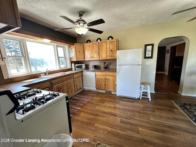 13862 Hartel Rd, Grand Ledge, MI 48837 - kitchen featuring white appliances, a sink, a ceiling fan, arched walkways, and dark wood-style floors