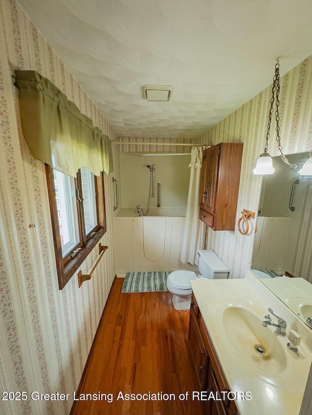 2278 Narrow Lake Rd, Charlotte, MI 48813 - bathroom with wallpapered walls, wood finished floors, toilet, vanity, and a tub