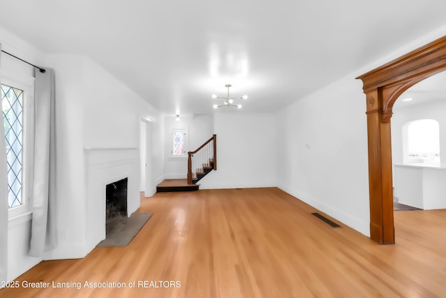 414 W St, Lansing, MI 48915 - unfurnished living room featuring a fireplace, light wood-style floors, arched walkways, stairway, and a chandelier