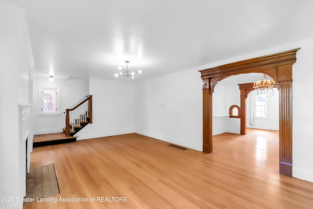 414 W St, Lansing, MI 48915 - unfurnished living room with a chandelier, light wood-style floors, stairway, and baseboards