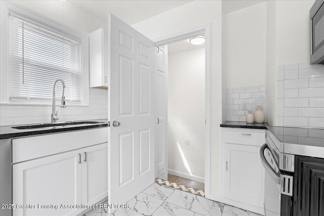 1200 W Rundle Ave, Lansing, MI 48910 - kitchen with a sink, dark countertops, light marble finish flooring, and white cabinetry
