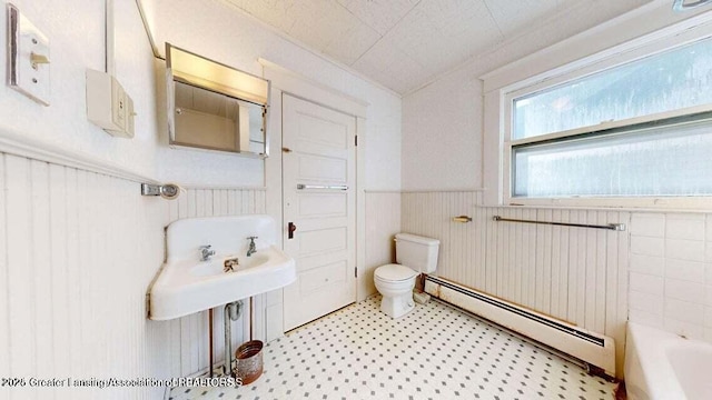 411 W Ionia St, Lansing, MI 48933 - bathroom featuring a baseboard heating unit, wainscoting, toilet, tile patterned floors, and a tub