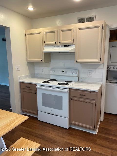 2303 Devonshire Ave, Lansing, MI 48910 - kitchen with electric range, under cabinet range hood, stacked washer / drying machine, light countertops, and dark wood finished floors