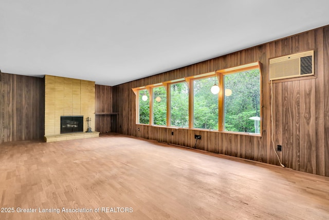 1450 N Hagadorn Rd, East Lansing, MI 48823 - unfurnished living room featuring a wall mounted AC, wood walls, a brick fireplace, and light wood-type flooring