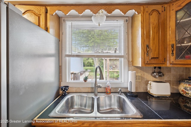 6187 Towar Ave, East Lansing, MI 48823 - kitchen with a sink, brown cabinets, freestanding refrigerator, dark countertops, and backsplash