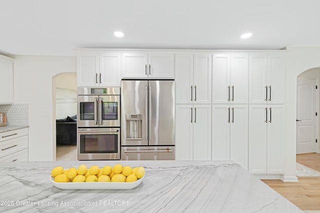1232 Chemung Forest Dr, Howell, MI 48843 - kitchen with appliances with stainless steel finishes, arched walkways, light stone countertops, white cabinetry, and recessed lighting