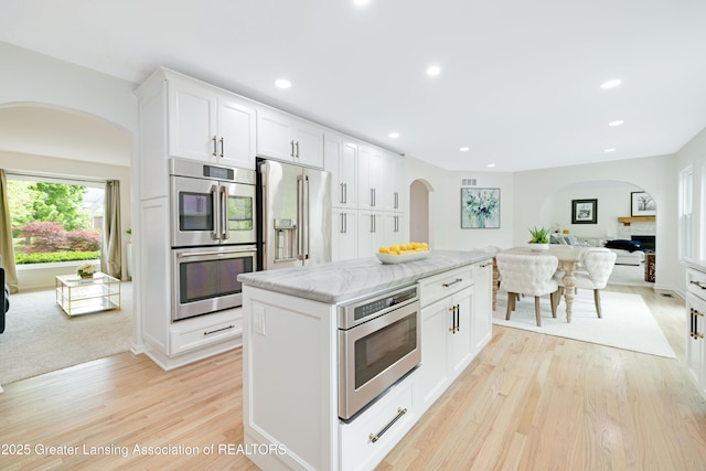 1232 Chemung Forest Dr, Howell, MI 48843 - kitchen featuring arched walkways, appliances with stainless steel finishes, open floor plan, light wood finished floors, and recessed lighting