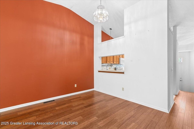 1101 Boulder Ct Unit 48, Lansing, MI 48917 - empty room featuring a chandelier, wood finished floors, baseboards, and high vaulted ceiling