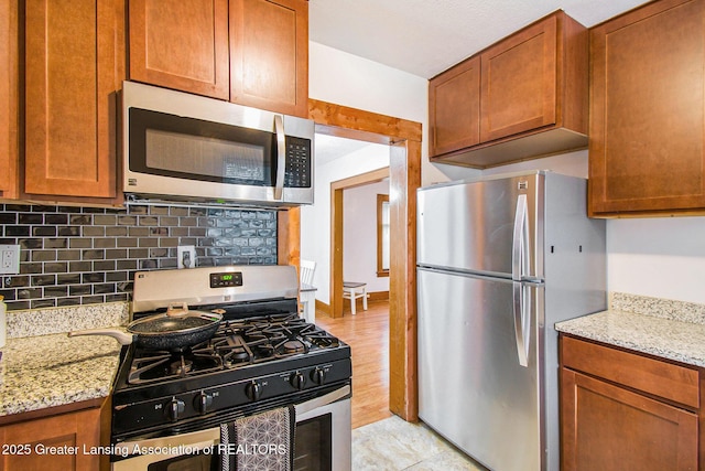 2104 Clifton Ave, Lansing, MI 48910 - kitchen featuring appliances with stainless steel finishes, tasteful backsplash, light stone countertops, and brown cabinets
