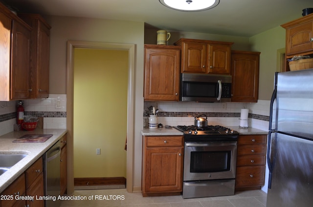 1161 Rebecca Rd, East Lansing, MI 48823 - kitchen with stainless steel appliances, light countertops, tasteful backsplash, and brown cabinetry