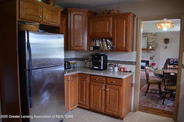 1161 Rebecca Rd, East Lansing, MI 48823 - kitchen featuring freestanding refrigerator, brown cabinetry, light stone counters, and backsplash
