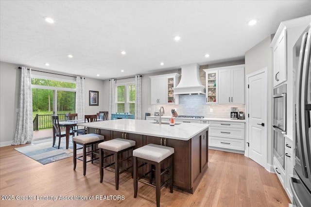 6619 Windford Ln, Grand Ledge, MI 48837 - kitchen with premium range hood, a sink, a kitchen island with sink, a kitchen bar, and decorative backsplash