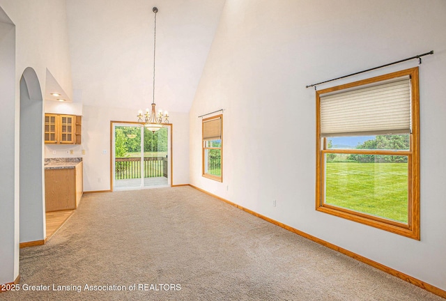 3037 Hawley Rd, Leslie, MI 49251 - unfurnished living room featuring high vaulted ceiling, baseboards, a chandelier, light carpet, and arched walkways