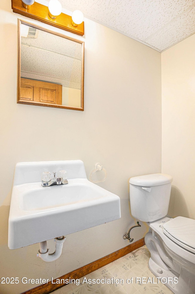 3037 Hawley Rd, Leslie, MI 49251 - half bathroom featuring toilet, a sink, baseboards, and a textured ceiling