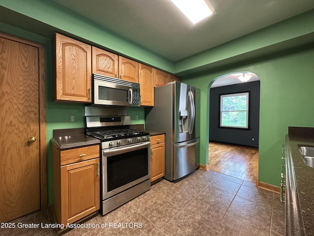 710 Gainsborough Dr, East Lansing, MI 48823 - kitchen featuring stainless steel appliances, dark countertops, arched walkways, and baseboards