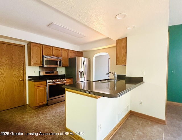 710 Gainsborough Dr, East Lansing, MI 48823 - kitchen with appliances with stainless steel finishes, dark countertops, a peninsula, arched walkways, and brown cabinetry