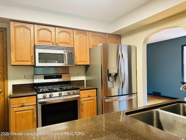 710 Gainsborough Dr, East Lansing, MI 48823 - kitchen with appliances with stainless steel finishes, arched walkways, and dark stone counters
