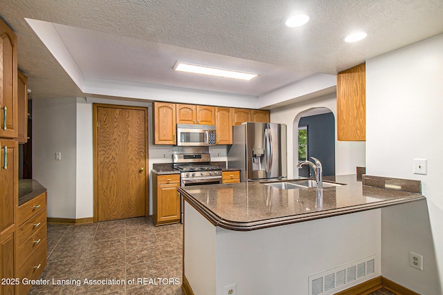 710 Gainsborough Dr, East Lansing, MI 48823 - kitchen featuring appliances with stainless steel finishes, a peninsula, arched walkways, brown cabinetry, and a textured ceiling