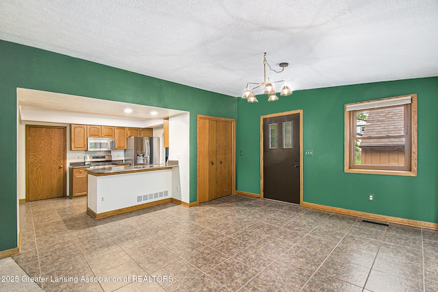 710 Gainsborough Dr, East Lansing, MI 48823 - kitchen featuring appliances with stainless steel finishes, a chandelier, brown cabinetry, a peninsula, and a textured ceiling