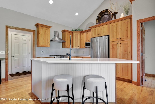 4740 Round Lake Rd, Laingsburg, MI 48848 - kitchen featuring appliances with stainless steel finishes, wall chimney exhaust hood, light wood-style floors, light countertops, and a kitchen breakfast bar