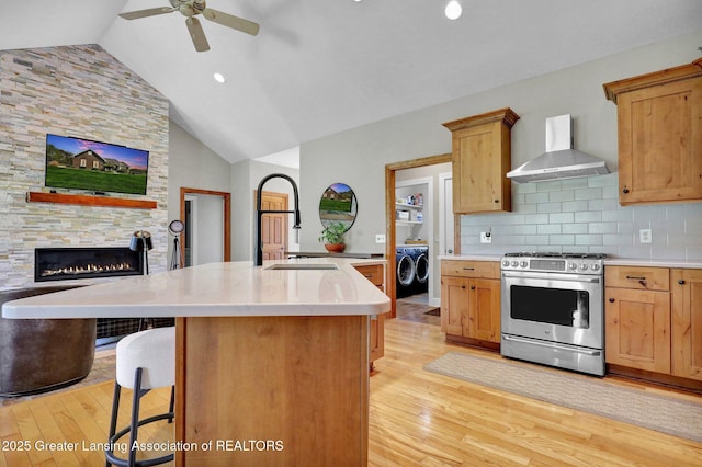 4740 Round Lake Rd, Laingsburg, MI 48848 - kitchen with stainless steel gas stove, wall chimney exhaust hood, light wood-style flooring, ceiling fan, and washer and dryer