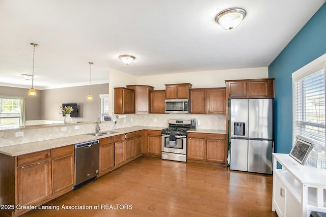 15145 Nottingham Fields Pkwy, Lansing, MI 48906 - kitchen featuring stainless steel appliances, a peninsula, decorative backsplash, light wood-style flooring, and hanging light fixtures