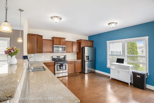 15145 Nottingham Fields Pkwy, Lansing, MI 48906 - kitchen featuring appliances with stainless steel finishes, a sink, brown cabinetry, hanging light fixtures, and tasteful backsplash