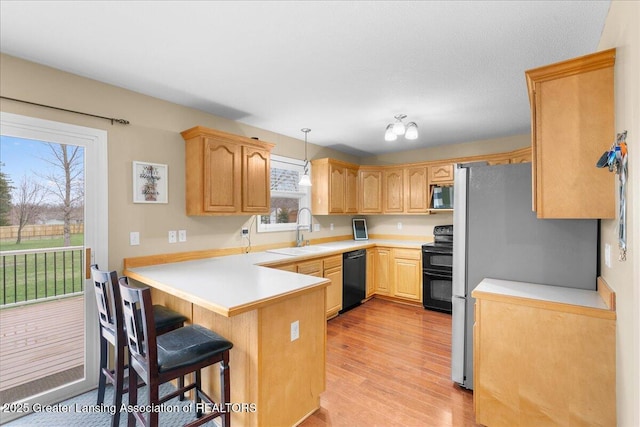 703 Hastay Blvd, Eaton Rapids, MI 48827 - kitchen with black appliances, a peninsula, a sink, light wood finished floors, and a breakfast bar