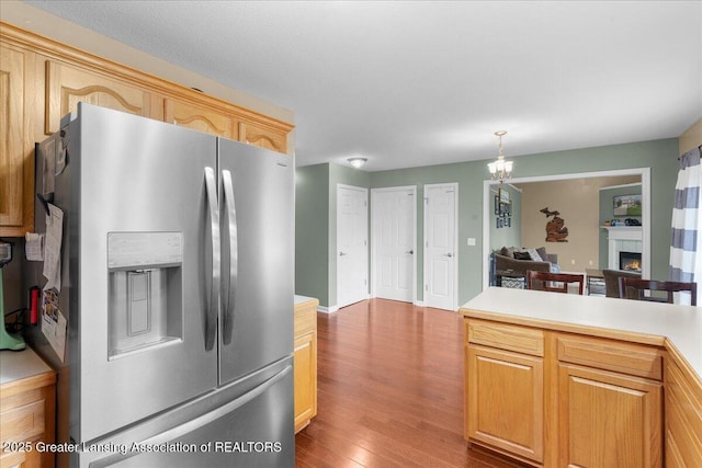 703 Hastay Blvd, Eaton Rapids, MI 48827 - kitchen with stainless steel refrigerator with ice dispenser, wood finished floors, light countertops, a chandelier, and a lit fireplace