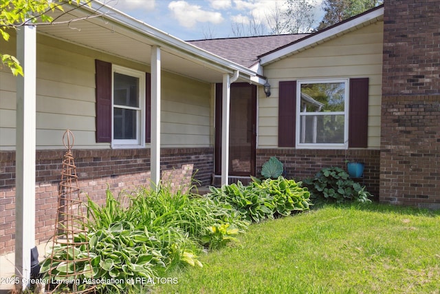7050 E Eaton Hwy, Sunfield, MI 48890 - view of exterior entry featuring brick siding, roof with shingles, and a yard