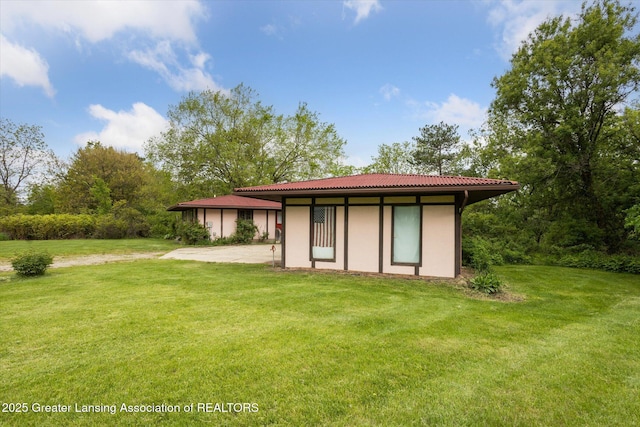 7161 E Eaton Hwy, Mulliken, MI 48861 - rear view of house with a yard, stucco siding, an outbuilding, and a tile roof