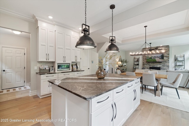 16851 Meadowbrook Dr, Haslett, MI 48840 - kitchen featuring stainless steel microwave, a center island, light wood finished floors, a stone fireplace, and ornamental molding