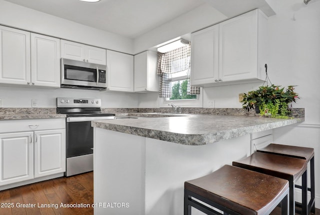 6415 Creyts Rd, Dimondale, MI 48821 - kitchen featuring appliances with stainless steel finishes, a peninsula, a breakfast bar, white cabinetry, and dark wood finished floors