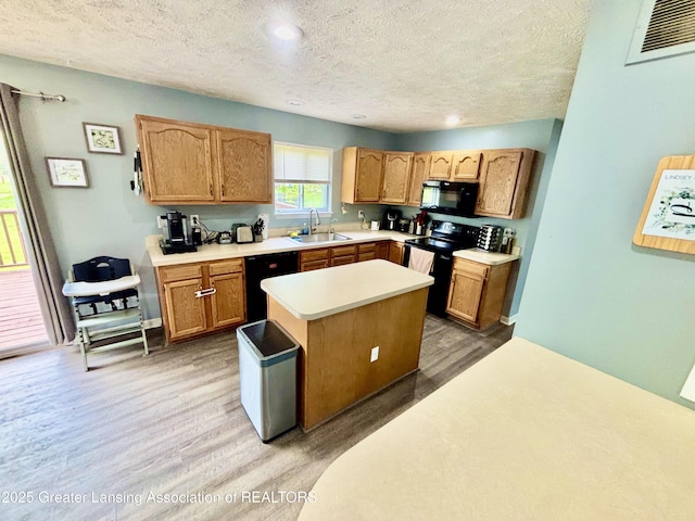 405 N Iris Ln, Laingsburg, MI 48848 - kitchen with black appliances, a sink, light wood-type flooring, a textured ceiling, and a kitchen island